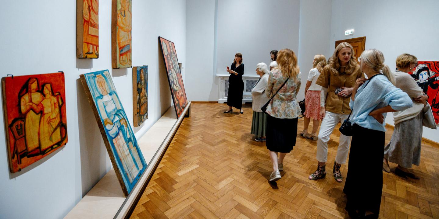 “Apciemotāji izstāžu zālē aplūko gleznas, kas izkārtotas uz sienām un novietotas uz zemiem podestiem; telpā valda mierīga un sarunām bagāta gaisotne.