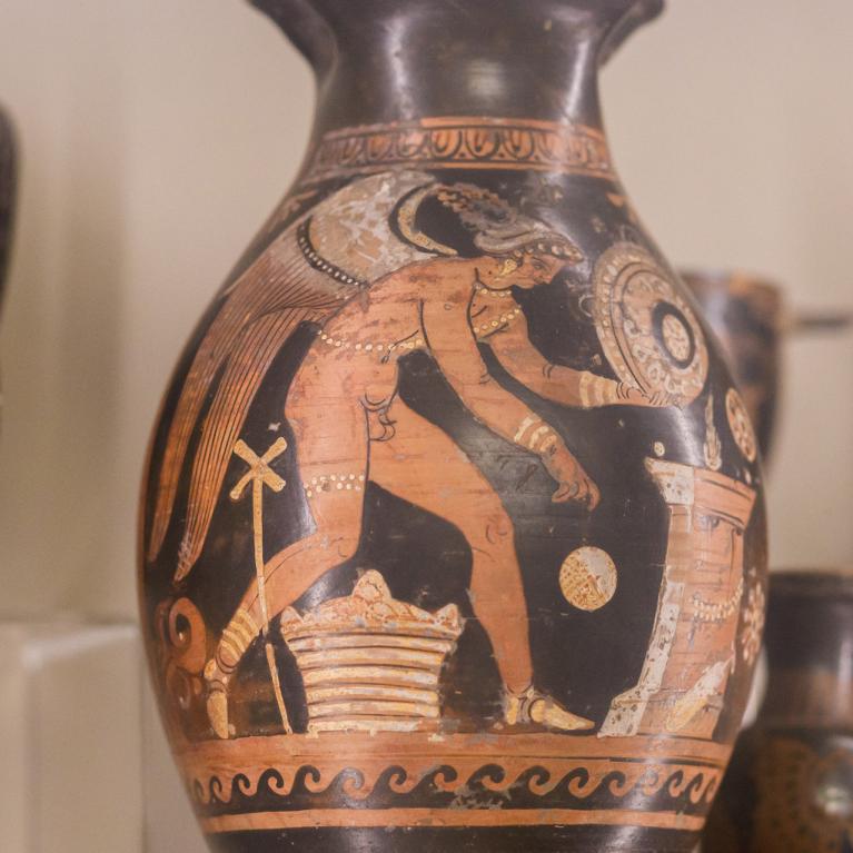 Antīkie grieķu keramikas trauki ar sarkanfigūru gleznojumiem, izstādīti vitrīnā.