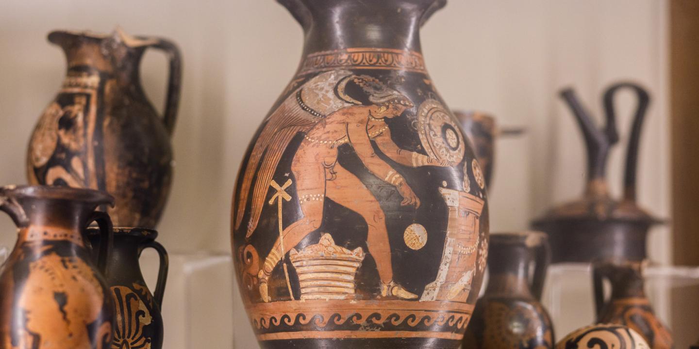 Antīkie grieķu keramikas trauki ar sarkanfigūru gleznojumiem, izstādīti vitrīnā.