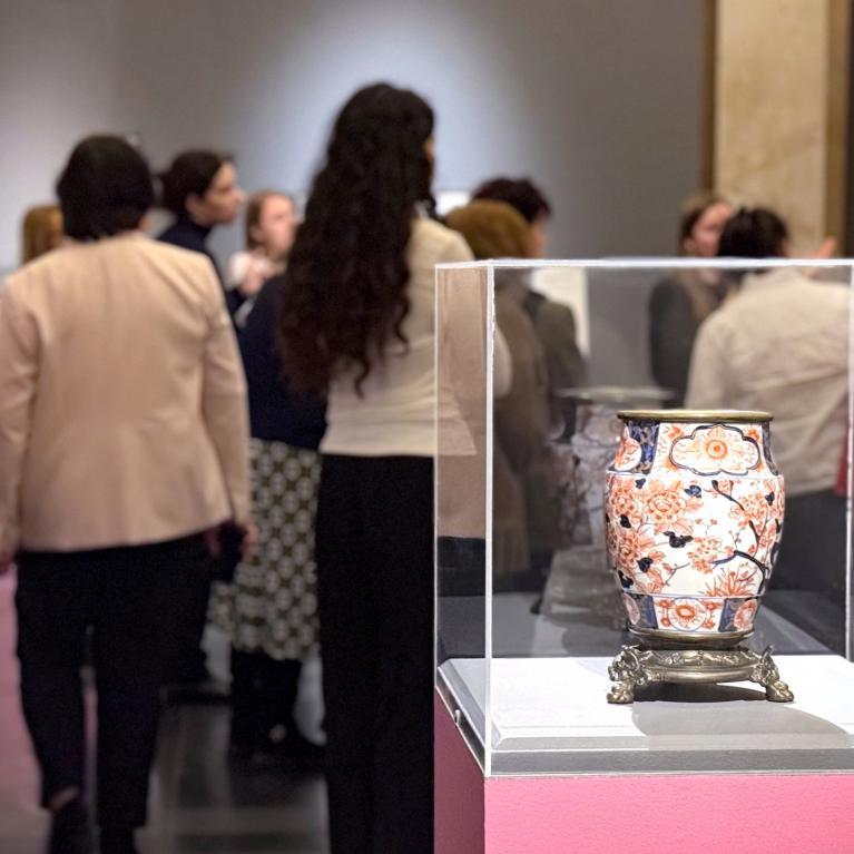 Japāņu grafikas darbs ar mūziķi, kas spēlē stīgu instrumentu, dekoratīvu rakstu un ziedu fonā.