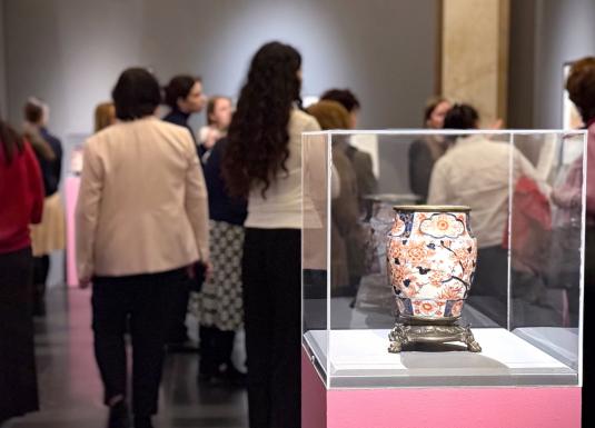 Japāņu grafikas darbs ar mūziķi, kas spēlē stīgu instrumentu, dekoratīvu rakstu un ziedu fonā.