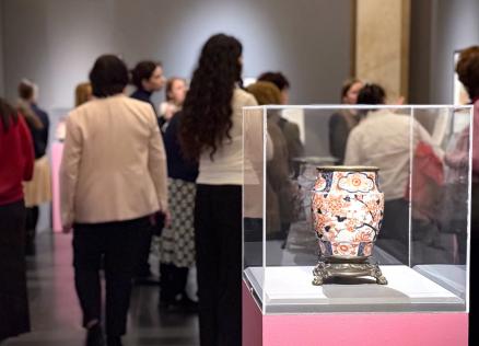 Japāņu grafikas darbs ar mūziķi, kas spēlē stīgu instrumentu, dekoratīvu rakstu un ziedu fonā.