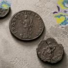 Trīs nolietotas senās monētas uz gaišas akmens virsmas, viena apaļa monēta ar stāvošu figūru centrā un divi saplīsuši fragmenti.