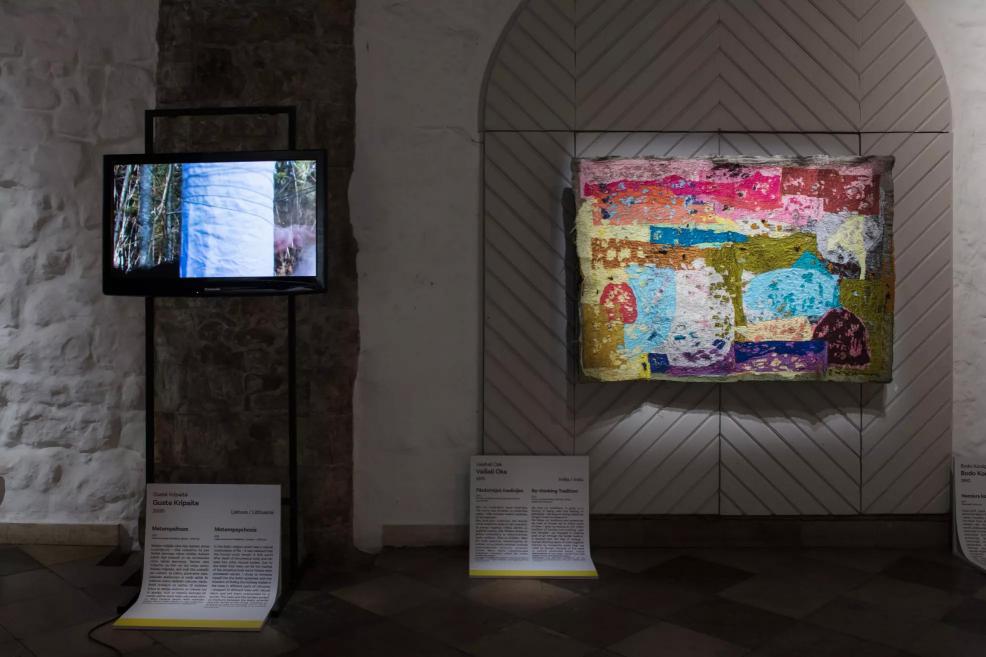 Video screen showing a tree image and a colorful mosaic-style textile work on the wall.