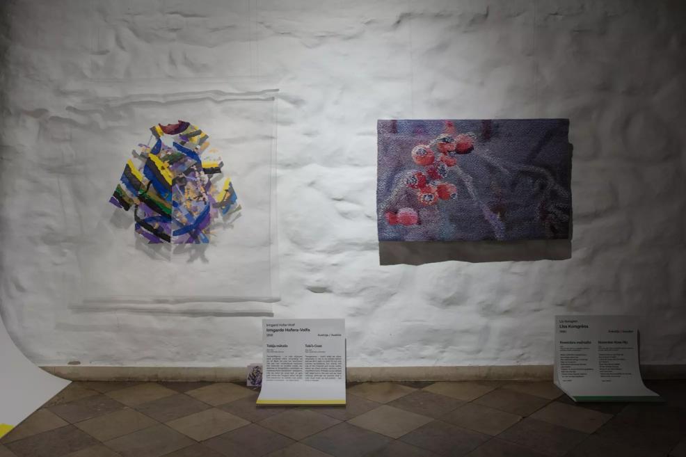 Two textile works on a white wall – an abstract composition in yellow and blue tones and a canvas with pink circular elements.
