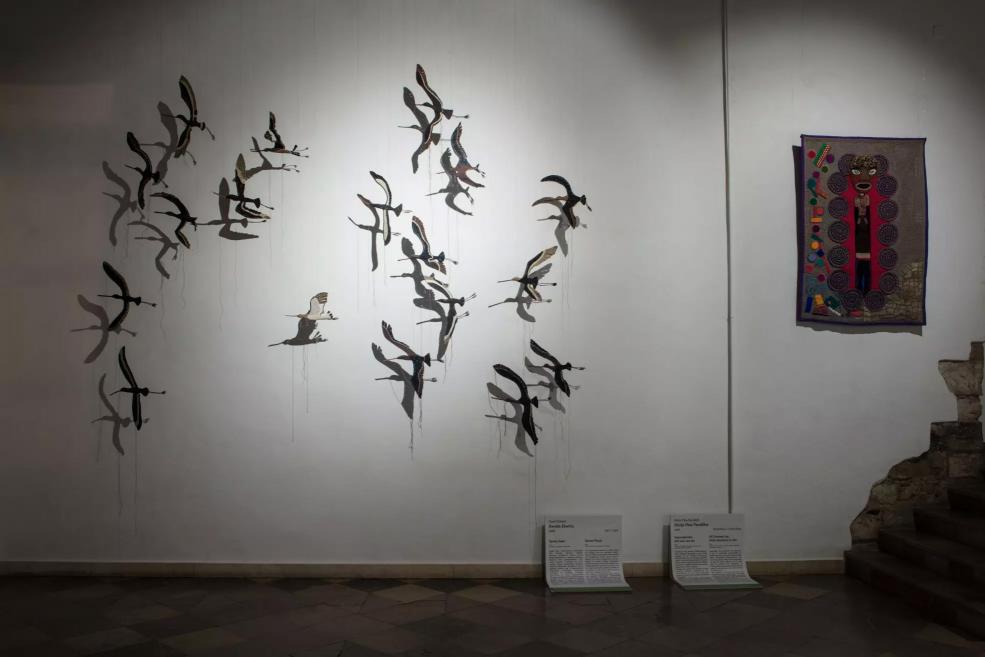 Wall composition with birds shown in flight and a colorful ornamental textile work.