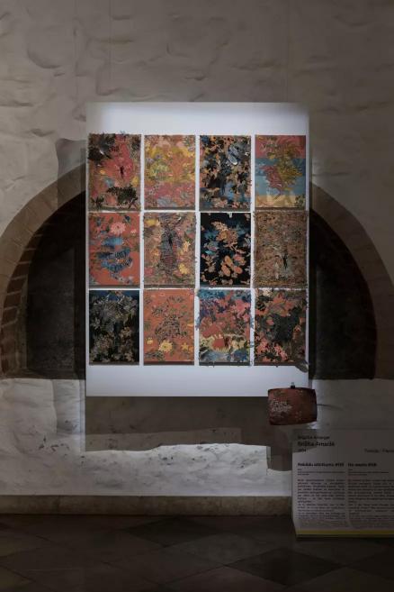A work of twelve panels with colorful floral and decorative patterns displayed on the wall.
