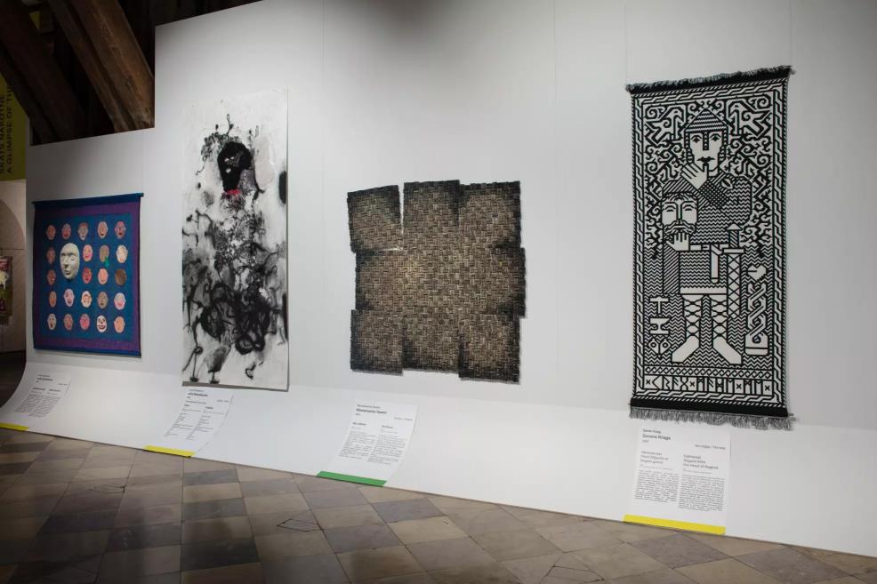 Four different artworks displayed on the wall – from a mask composition and abstract painting to a geometric weave and a black-and-white figurative tapestry.