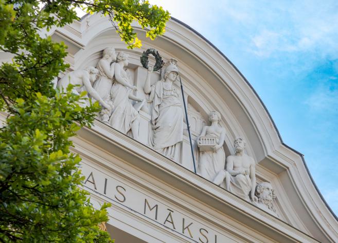 Apmeklētāju grupa muzejā stāv pie sienas un aplūko gleznu ar sievieti un bērniem.