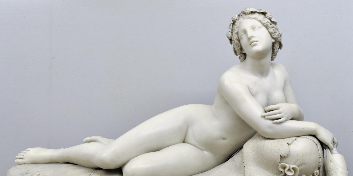 A marble sculpture of a reclining female figure wearing a wreath of grapes in her hair.