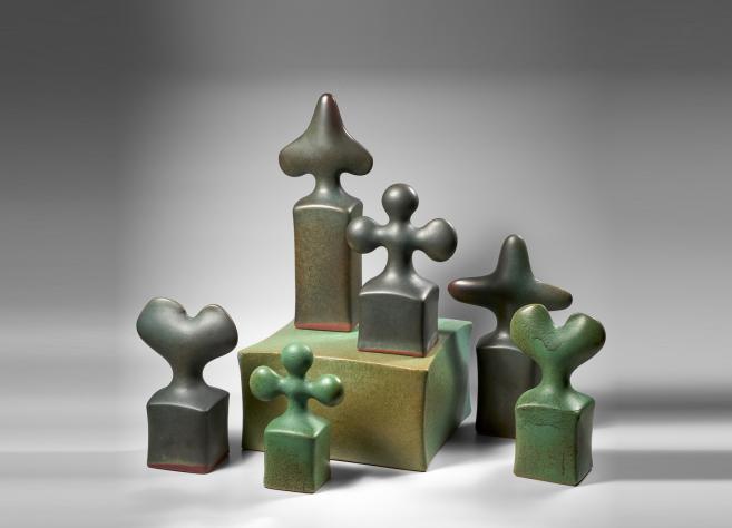 A group of ceramic sculptures arranged on a block-like pedestal, with stylized cross- and finial-shaped tops in green and gray tones.