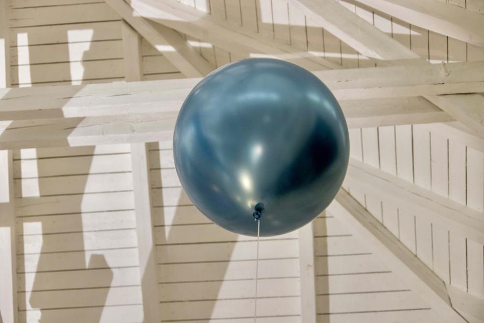 Zils balons ar auklu pie gaišas koka sienas ar šķērssijām un ēnām.