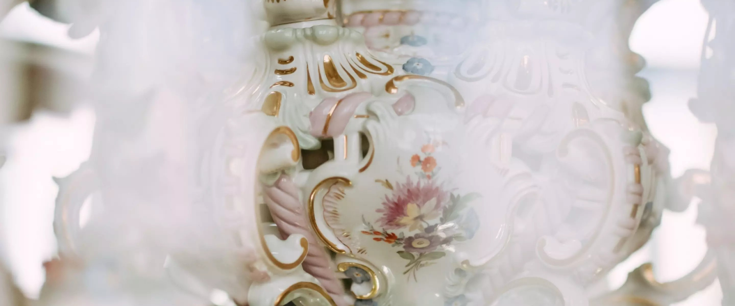 Close-up of a white porcelain decorative detail with gilding, pastel-coloured ornamentation and a painted floral composition.