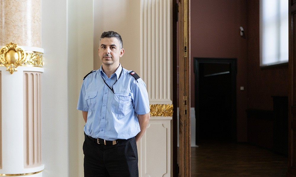 The image shows a museum security guard in uniform standing by a doorway inside the museum.