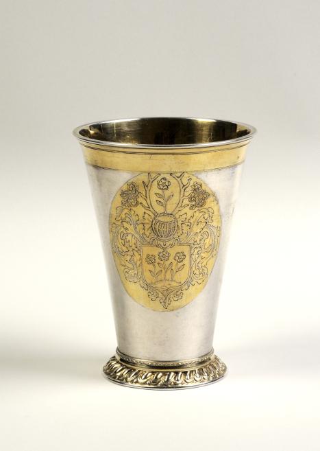 Silver goblet with a gilded rim, decorative coat of arms and ornate foot on a light background.
