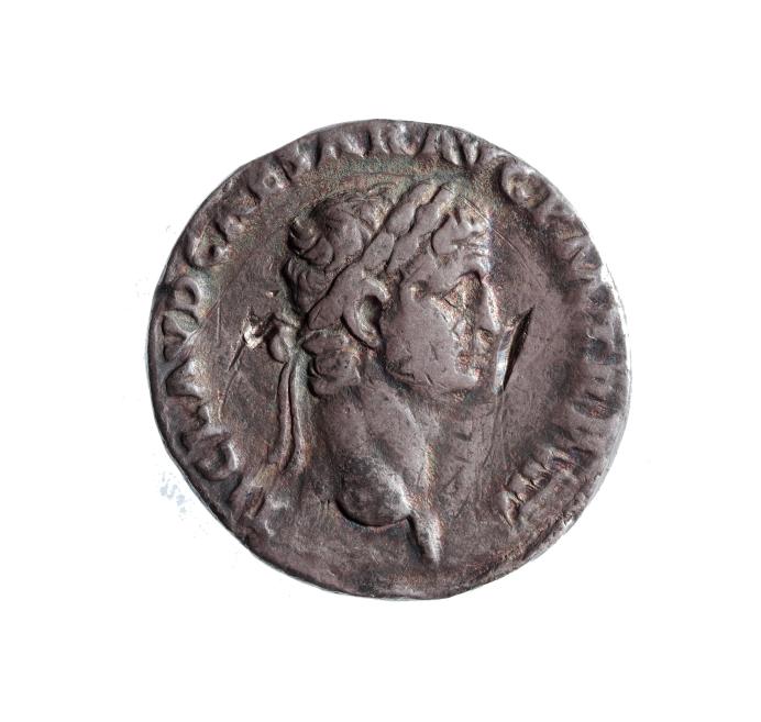 Coin with a relief profile of a lion’s head and surrounding inscription on a worn metal surface against a white background.