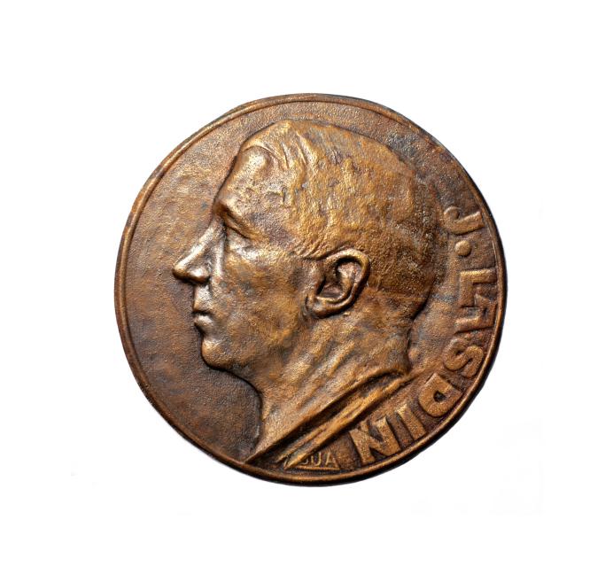 Bronze medal with a male profile relief on a white background, with an inscription visible along the right edge.