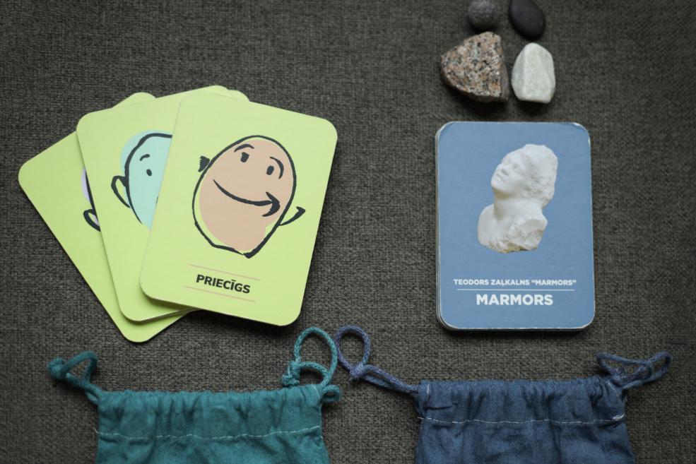 Emociju kartītes ar smaidīgu seju un marmora paraugu karti uz pelēka auduma.