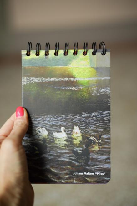 Blociņš ar gleznu reprodukciju, kurā redzamas pīles uz ūdens.