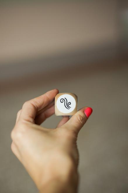 Rokā turēts koka kauliņš ar melnu ornamentu uz baltas uzlīmes.