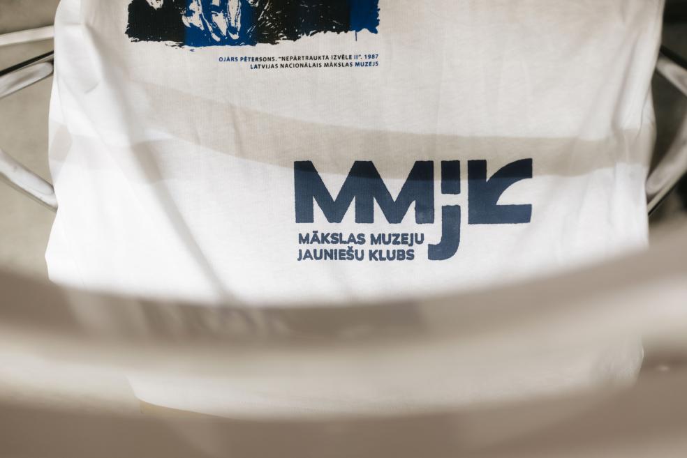 Baltas T-krekla apdruka ar Mākslas muzeju Jauniešu kluba logo.