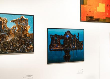 Muzeja sienā izkārtotas četras krāsainas abstraktas gleznas dažādos formātos ar izteiktiem zilas, sarkanas un zeltainas krāsas laukumiem.