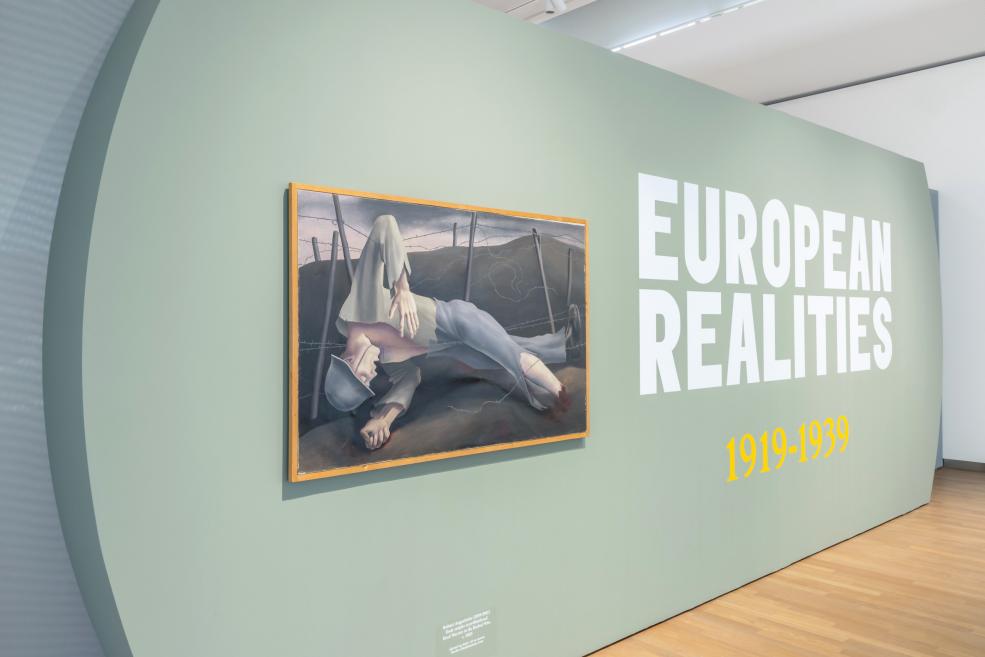 Izstādes sienā iebūvēts gleznojums ar ievainotu karavīru blakus uzrakstam “European Realities 1919–1939”.