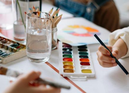 Uz galda redzamas akvareļu krāsas, otas un zīmuļi bērnu radošajā darbnīcā.