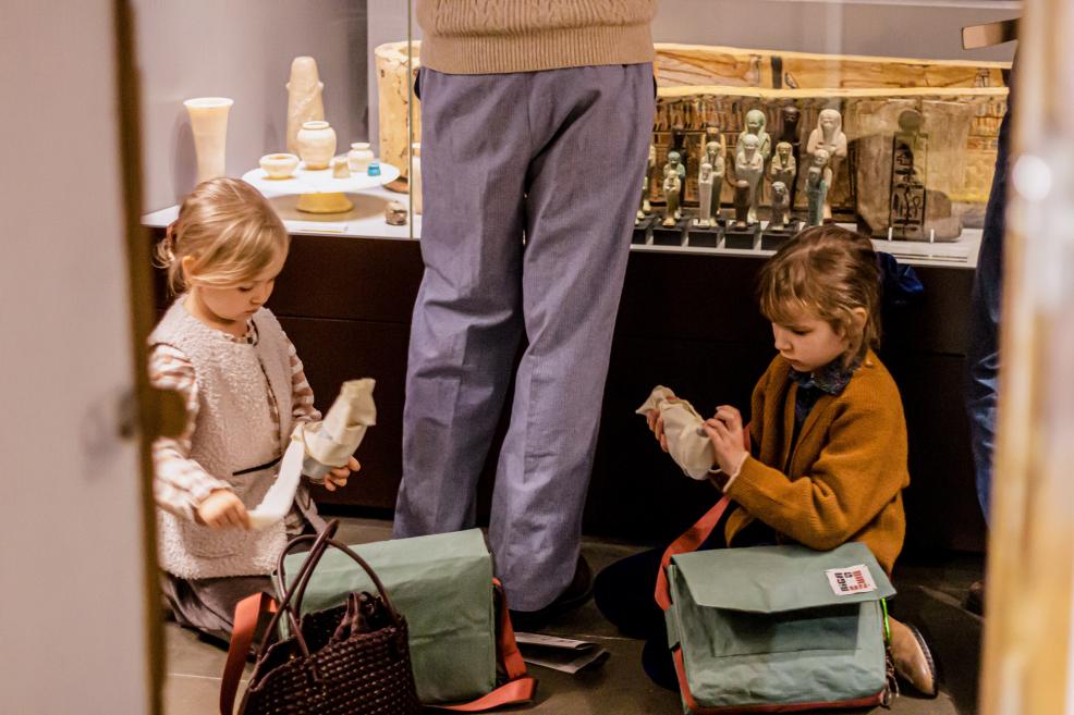 Divas meitenes ar ceļojuma somām pēta priekšmetus pie muzeja vitrīnas.