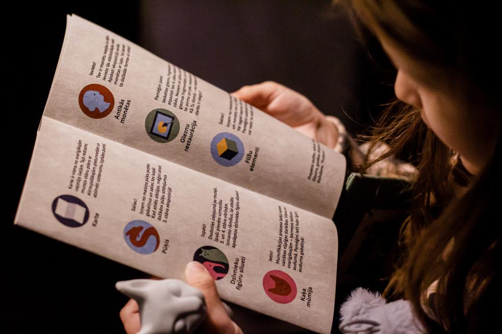 Meitene tur bukletu ar uzdevumiem muzeja apmeklējumam.