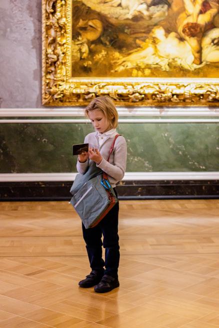 Zēns ar somu skatās karti vai bukletu gleznas priekšā.