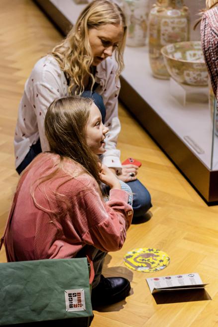 Sieviete un meitene pilda uzdevumu pie muzeja vitrīnas.