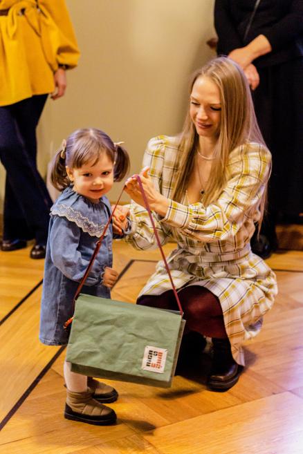 Sieviete pasniedz dāvanas maza vecuma meitenei muzeja pasākumā.