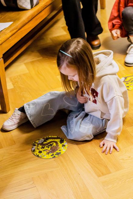 Meitene sēž uz grīdas un skatās uz pabeigtu puzli ar pūķi.