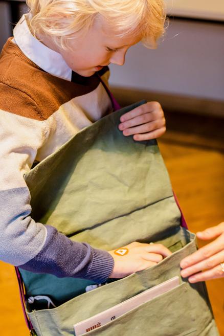 Zēns pēta saturu zaļā somā ar uzrakstu “Rīgas Birža”.