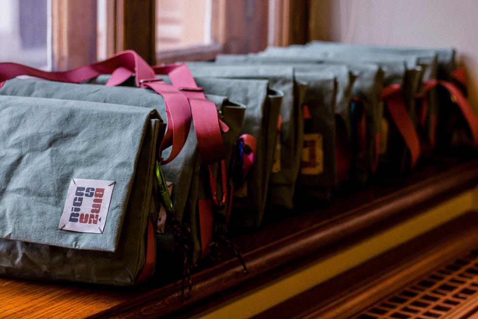 Zaļas auduma somas ar uzrakstu “Rīgas Birža” rindā uz palodzes.