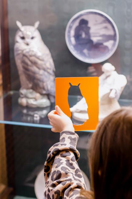 Meitene tur oranžu rāmīti ar pūces siluetu vitrīnas priekšā.