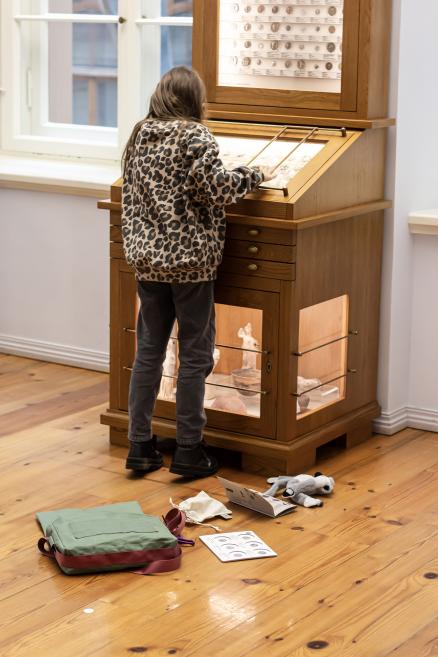 Meitene leopardraksta džemperī pēta monētu vitrīnu muzejā.