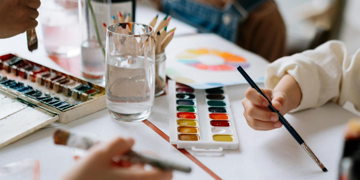 Uz galda redzamas akvareļu krāsas, otas un zīmuļi bērnu radošajā darbnīcā.