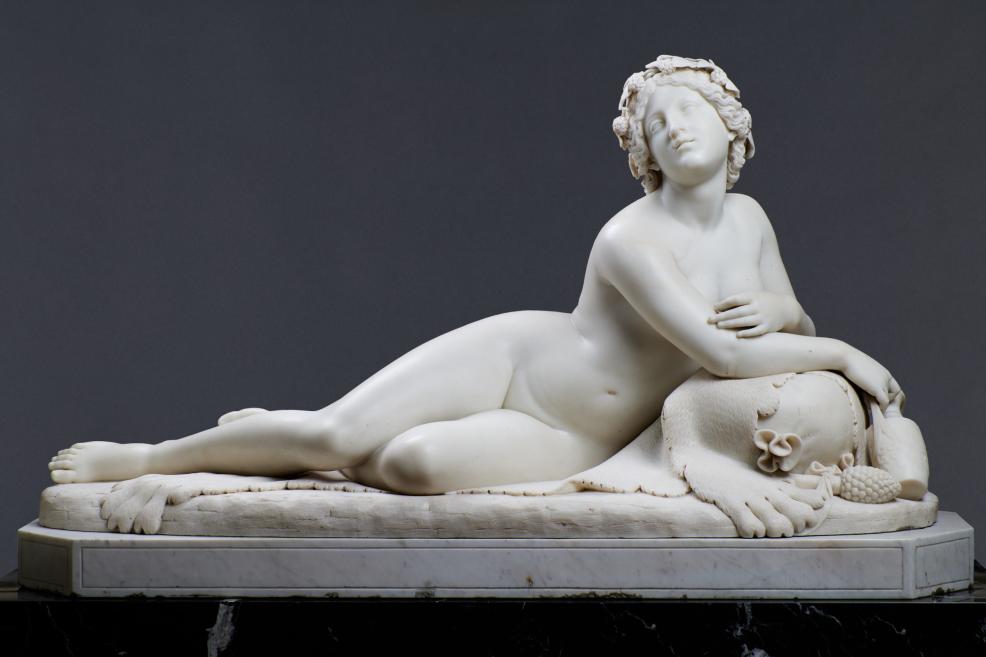 White marble sculpture of a reclining female figure on a pedestal against a dark background.
