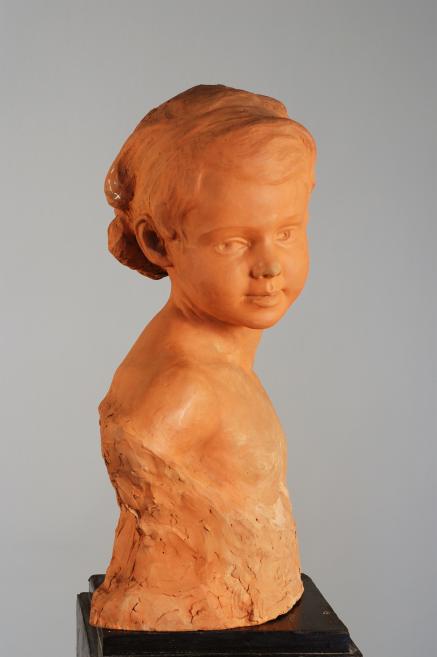 Terracotta bust of a young girl’s head and shoulders on a dark pedestal against a gray background.