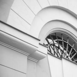 Black and white architectural detail featuring a semicircular window and decorative plaster lines.