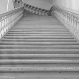 Black and white view of a wide wooden staircase with a balustrade in a historic building.
