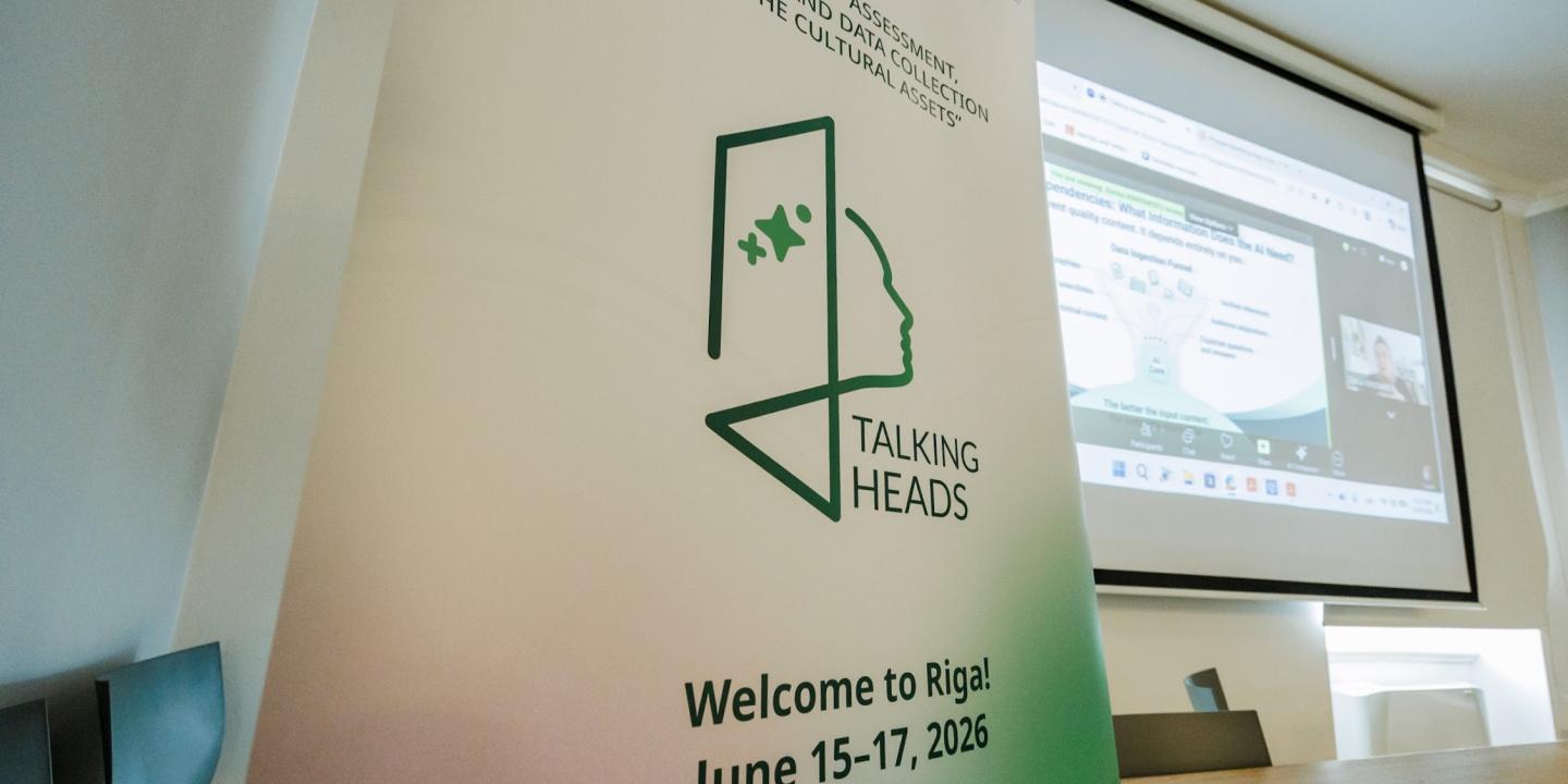 Vertikāls pasākuma baneris ar uzrakstu Workshop Assessment Mapping and Data Collection of the Cultural Assets un Talking Heads, konferenču zālē pie ekrāna ar prezentāciju.
