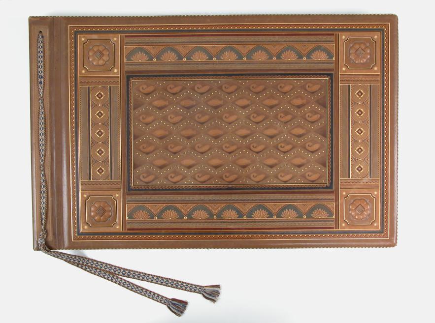 Dekoratīvs brūnas ādas albums ar reljefiem ģeometriskiem un ziedu ornamentiem un divām pušķotām lentēm.