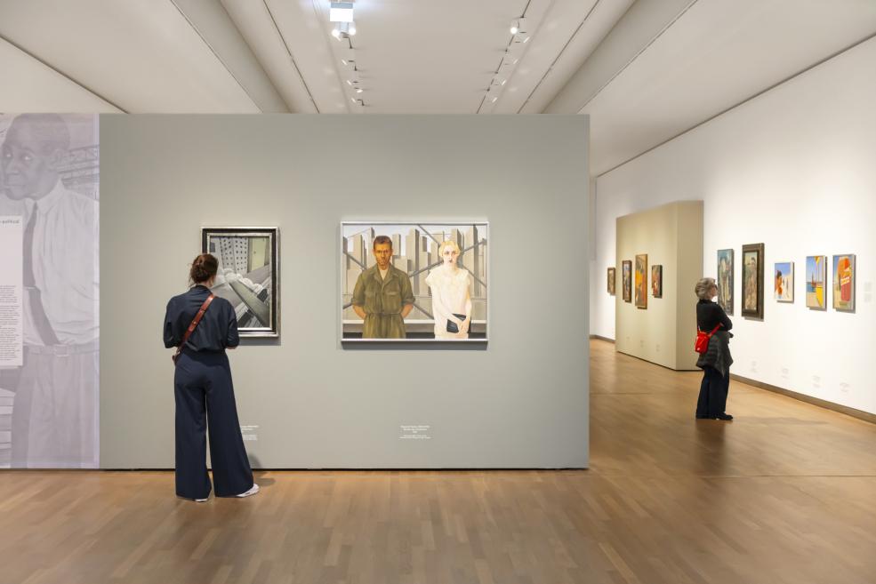 Divi apmeklētāji aplūko modernisma gleznas baltā izstāžu zālē, fonā redzams “European Realities” ekspozīcijas ievads.