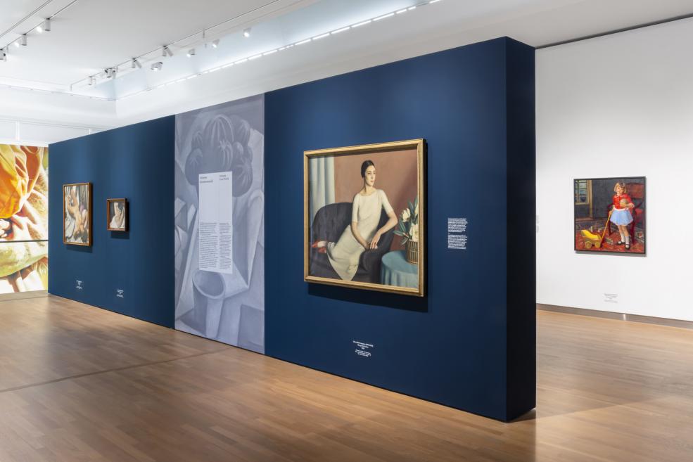 Uz tumši zilas izstāžu sienas eksponētas vairākas klusās dabas un modernisma gleznas.