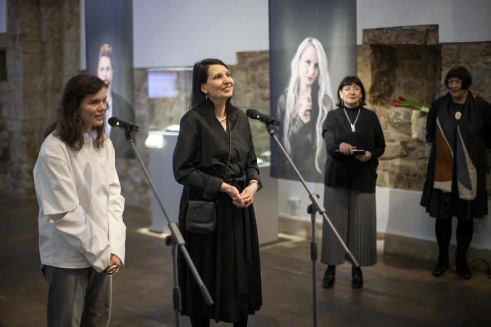 Two women speak into microphones at a jewelry exhibition