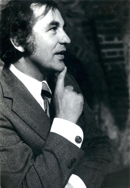 Black-and-white profile portrait of a man wearing a suit and touching his chin with a raised hand.
