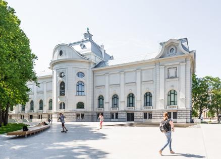 Gaiša, vēsturiska muzeja ēka parkā, priekšā redzami cilvēki, kas pastaigājas un atpūšas.